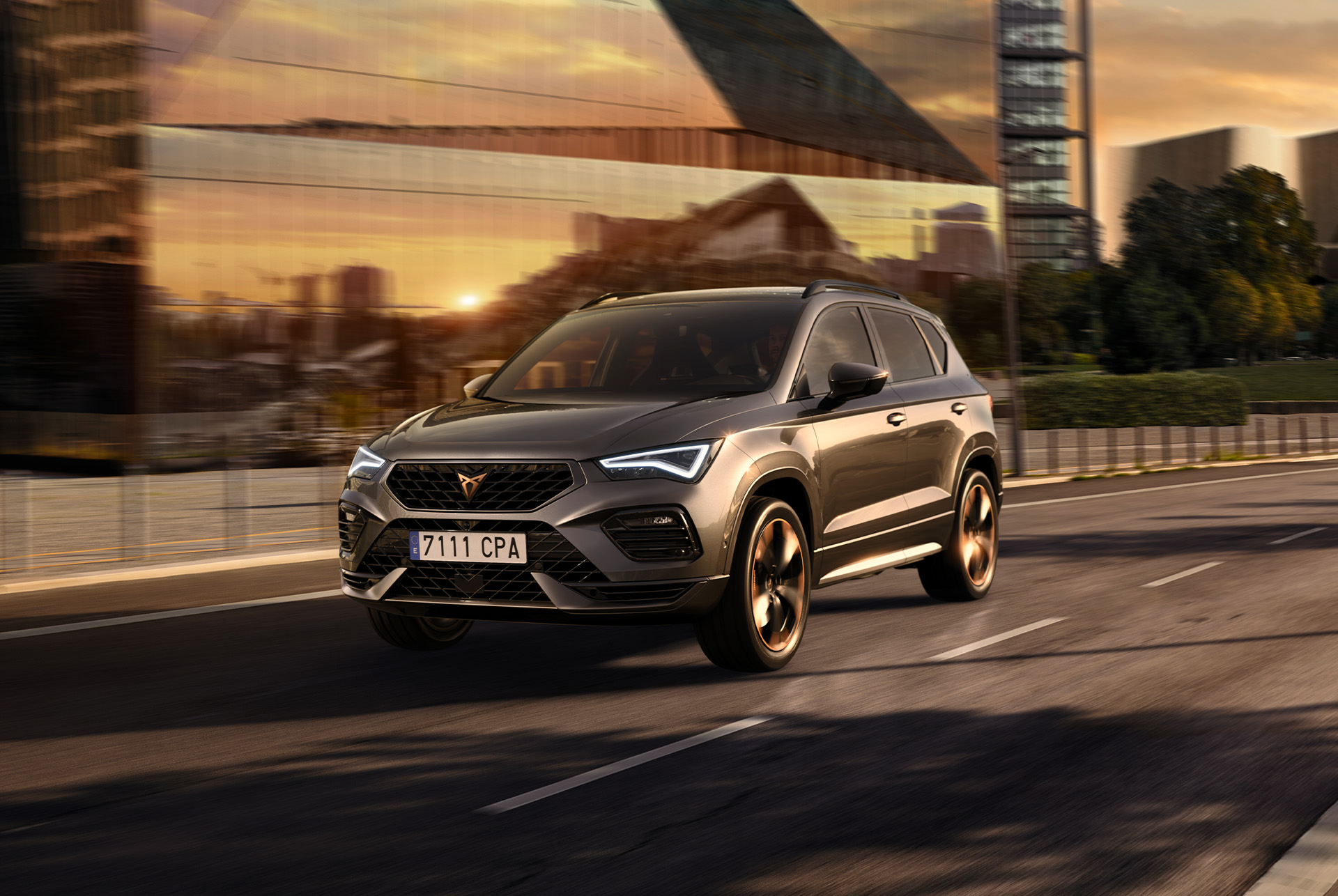 Pelēks CUPRA Ateca SUV uz balta fona. Automobilim ir izteiksmīgs priekšējais režģis, LED priekšējie lukturi un vieglmetāla diski ar vara akcentiem, kas izceļ tā sportisko dizainu.