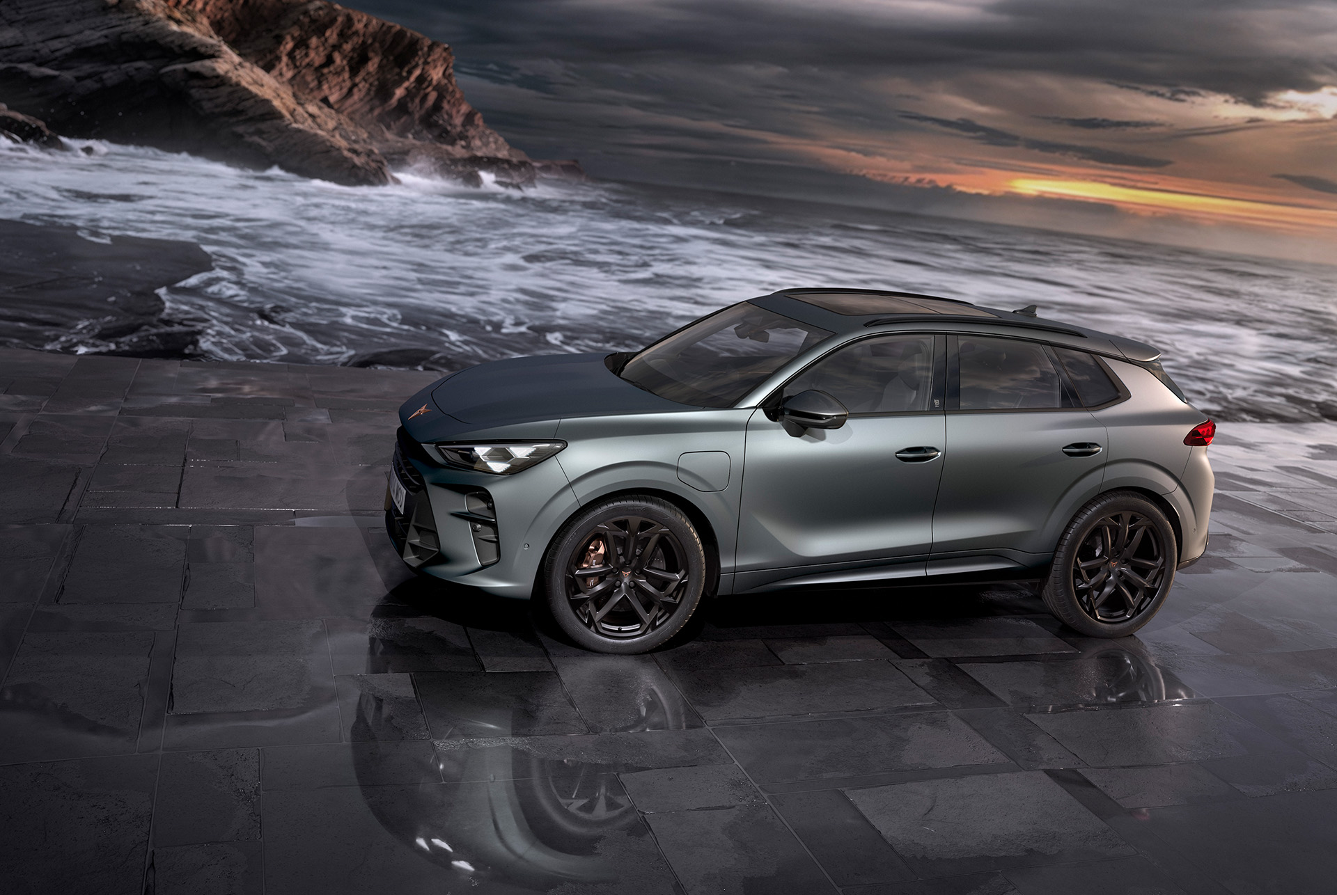 cupra terramar hibrīda suv, jaunais 2024. gada modelis, skats no sāniem, 20 collu america’s cup vieglmetāla diski un akebono bremzes, enceladus grey matt krāsa, uz slapja asfalta pie jūras saulrietā. 